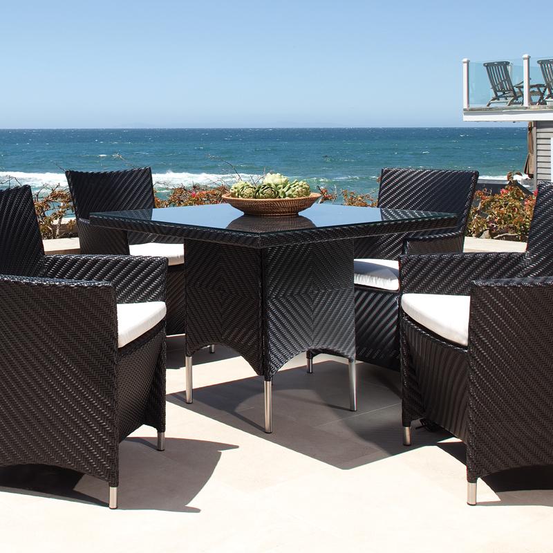 alt="32002BK Valencia 40 inch Square Wicker Table with decorative bowl on glass table top and 4 Valencia side chairs on outdoor terrace overlooking ocean with house in background"