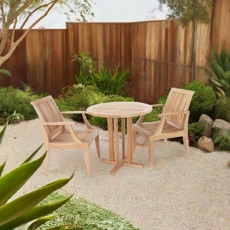 alt="70298 Laguna Teak 3 pc Bistro Set of a Teak Bistro 30 inch Round Table and 2 Laguna Teak Dining Armchairs angled on a stone path with landscape plants and fence in the  background"