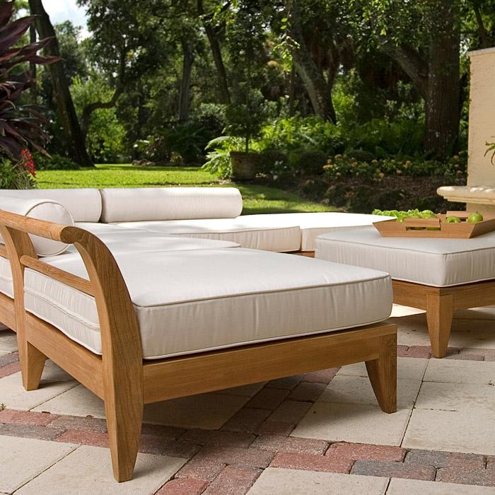 alt="16766 Aman Dais Sectional Set side angled view with bolsters and cushions and a teak serving tray with green apples on an ottoman on a paver patio with a landscaped background"