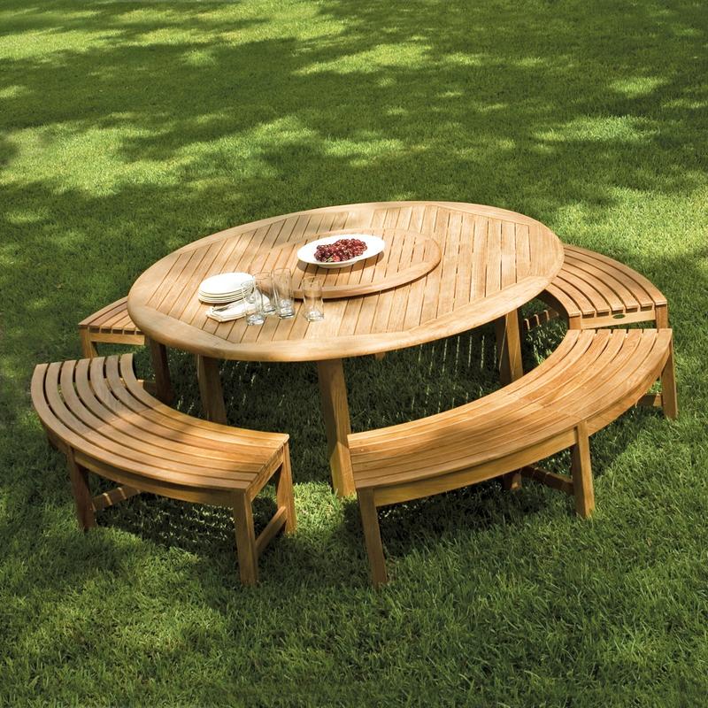 alt="70090 Buckingham Picnic Dining Set showing teak lazy susan with bowl of grapes in center umbrella hole and stack of plates silverware napkins on grass field"