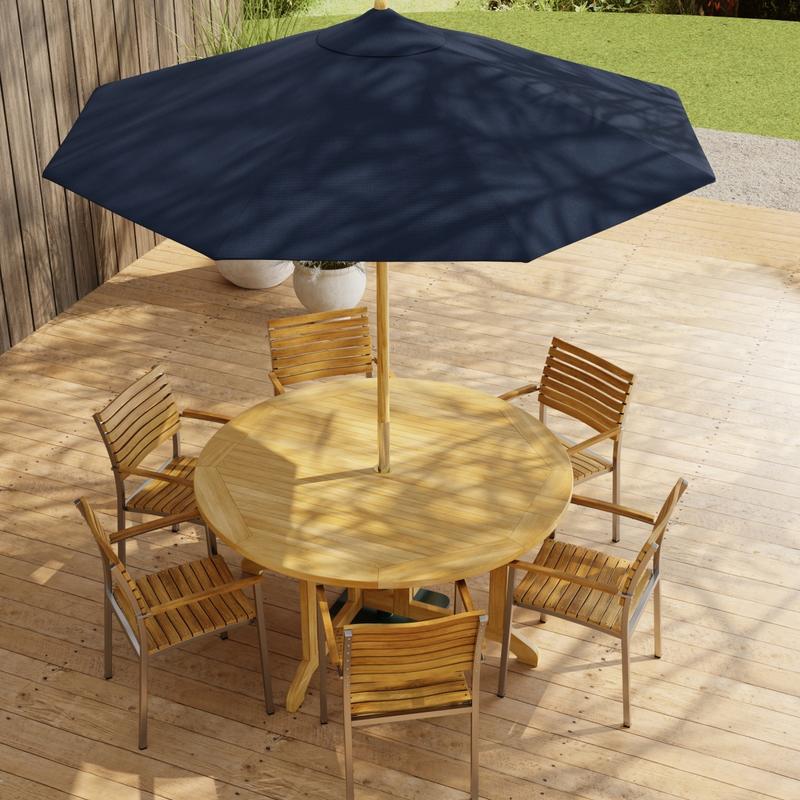 alt="70349 Barbuda Vogue Teak 7 pc Dining Set with optional umbrella in angled aerial view on paver patio with wood privacy wall with landscaping plants and trees in background"
