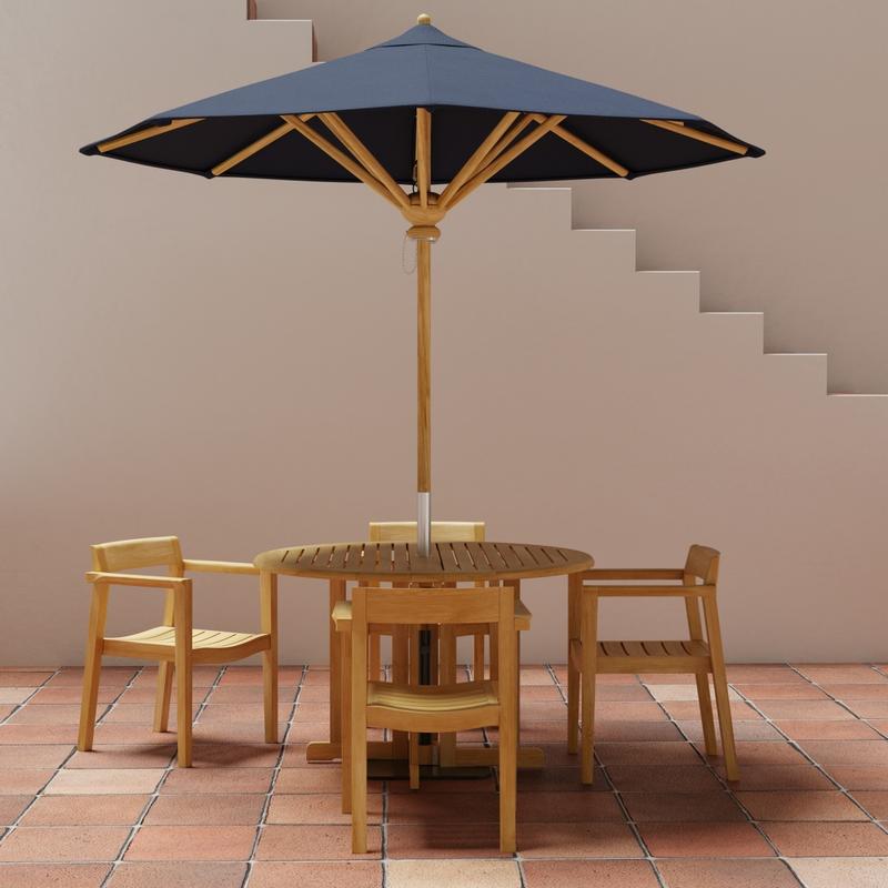alt="70384 Barbuda Horizon teak round folding dining table and 4 Horizon Dining Armchairs with optional umbrella in table center in side view on stone patio with staircase in background"