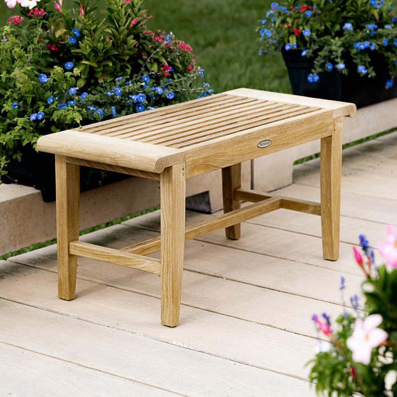 alt="13068 Laguna teak 3 foot long Backless Bench on a stone walkway with flowers and shrubs in background"