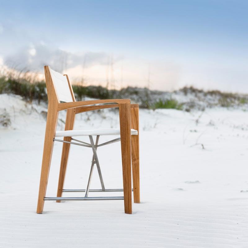 alt="70618 Odyssey Folding Chair in Marine Sealant Finish on sandy beach facing ocean with sea grass and sunset sky in background"