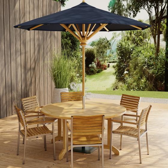 70349 Barbuda Vogue Teak 7 pc Dining Set with optional umbrella on paver patio with wood privacy wall with landscaping plants and trees in background