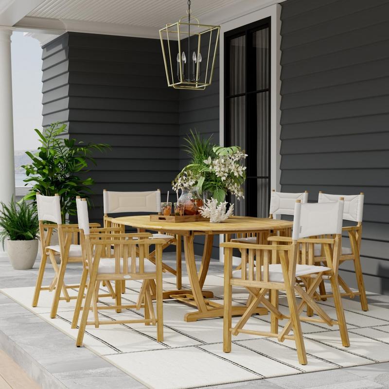 alt="70079 Martinique Director Chair 7 piece Oval Dining Set side view on patio with potted plants and hanging gold light fixture above table and potted plants and house with glass door in background"