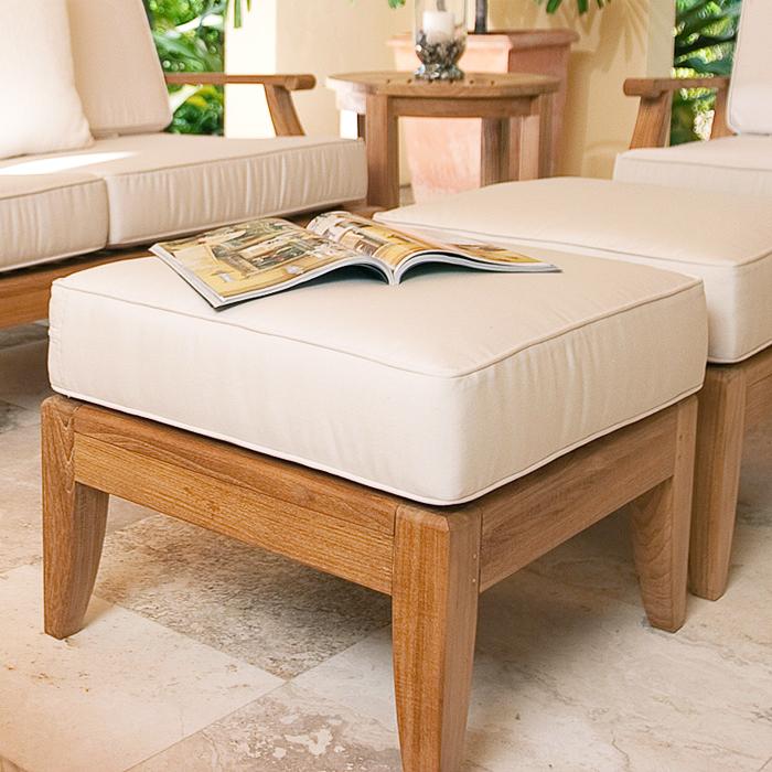 18652 Laguna sofa set on tile patio close up of two cushioned ottomans an opened magazine and side table with candle and background of green shrubs