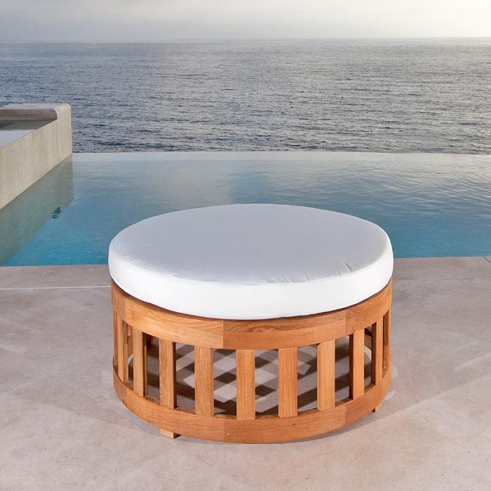 alt="14171 Kafelonia 36 inch Teak Coffee Table Ottoman with cushion side view on stone patio with an infinity pool ocean and blue sky in background"
