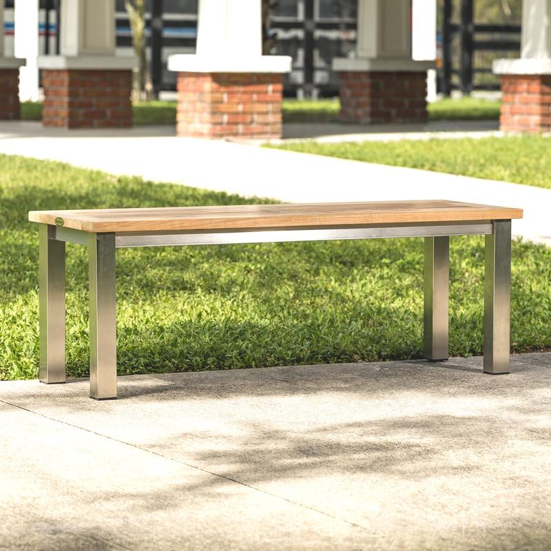 alt=" 23940 Vogue teak and stainless steel 4 foot backless bench on concrete walkway with grass and house in background"