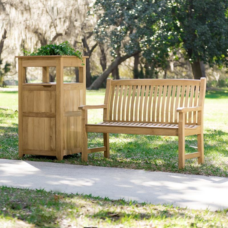 alt="13218 Veranda Teak 4 foot Bench beside teak trash receptacle on grass field with concrete walkway in front and trees in background"