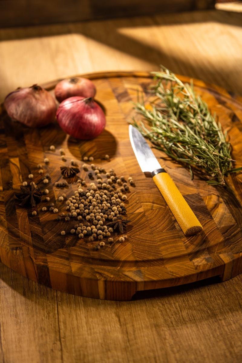 alt="19122 Butcher Block 15 inch Round Charcuterie Cutting Board with rosemary and 3 red onions and whole black pepper and a knife with yellow handle  aerial view on a counter top"