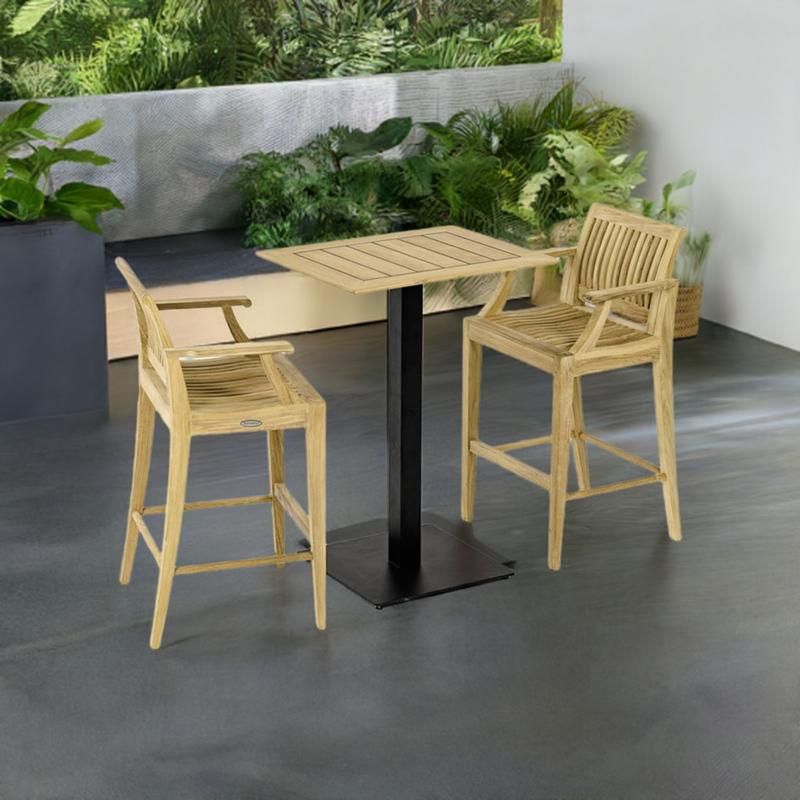 alt="70642  Laguna Barstool 3pc Teak Bar Set of Rectangular Teak Table Top on Black Gar Base and 2 Laguna Barstools angled on outdoor patio with plants and privacy wall and trees in background"