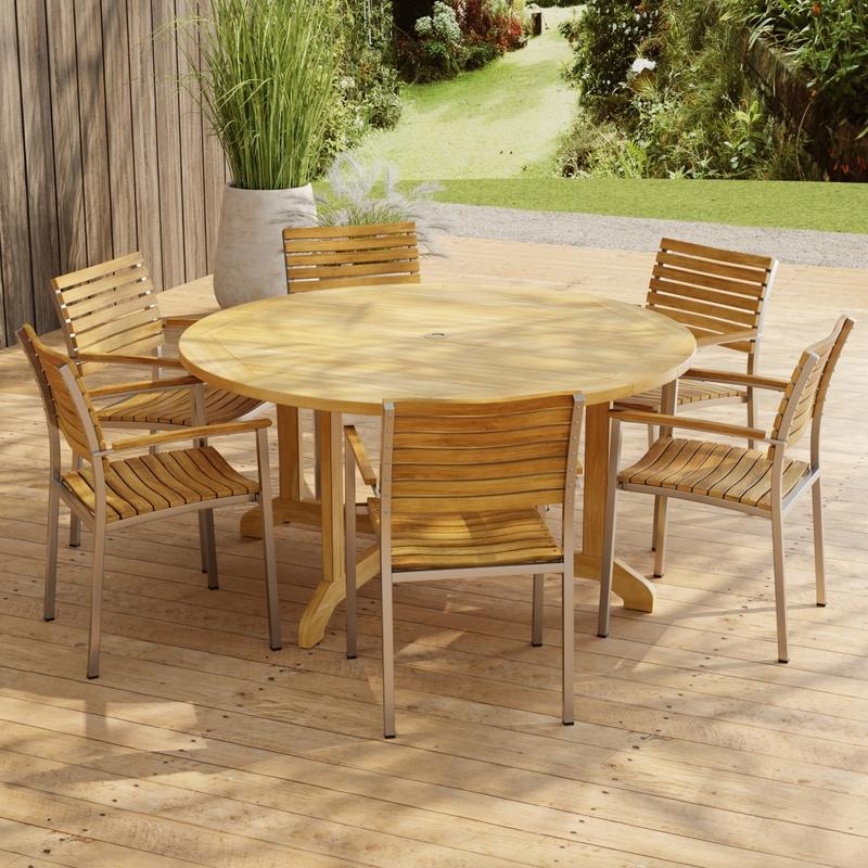 alt="70349 Barbuda Vogue Teak 7 pc Dining Set in angled side view on paver patio with wood privacy wall with landscaping plants and trees in background"