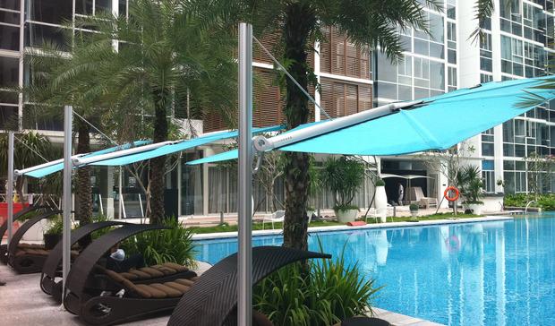 alt="sp2590set spectra solo umbrella and paver base showing angled side view of three over lounge chairs on pool deck facing pool with landscaping trees and hotel in background"