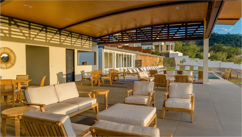 alt="70905 Laguna Maya 8 pc Sofa Set on patio aerial view with two pillar candles in glass holders on side tables open magazine on ottoman potted palm landscaped grass area in background"