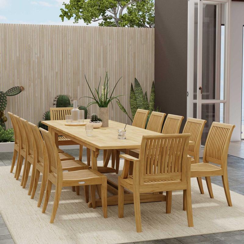 alt="70300 Grand Laguna 13 pc Teak Dining Set with Grand Veranda Dining Table and 12 Laguna Side Chairs on patio next to a house and a fence with plants in the background"
