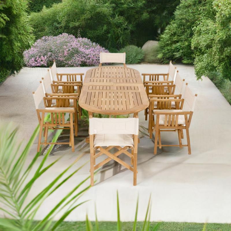 alt="70015 Montserrat Director 9 piece teak Dining Set end angled view on concrete patio surrounded by landscaping plants and trees in the background"