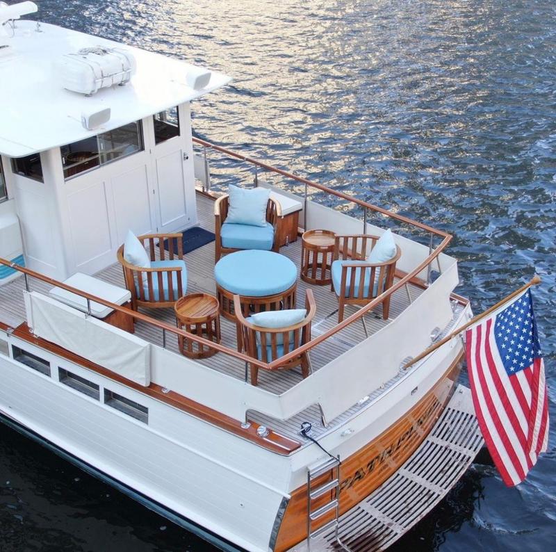 alt="Kafelonia 7 piece Lounge Set with marine gloss finish  two cushioned teak storage bins on a boat deck with American flag on back of boat on water"
