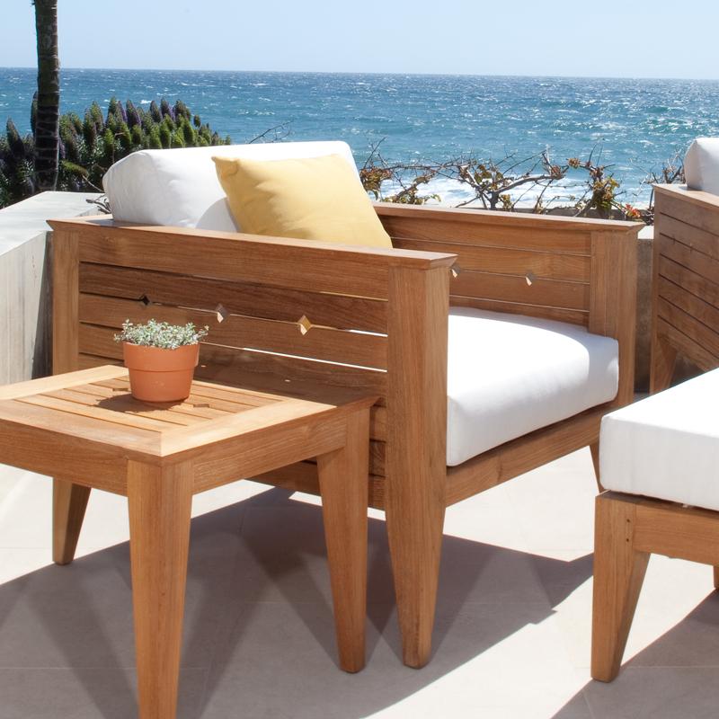 alt="12160dp Craftsman teak armchair set cushions and throw pillow potted plant on end table outside on concrete terrace with flora and ocean background"