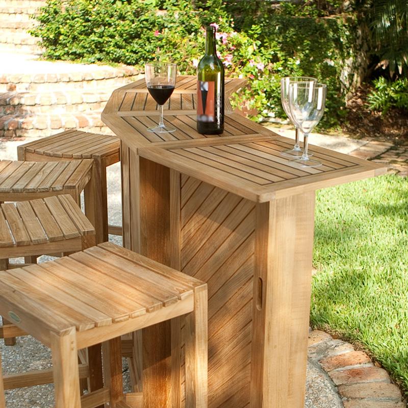 alt="70084 somerset teak bar set fully opened showing three wine glasses and wine bottle on bar top displayed on patio with potted plants stone steps vegetation in background "