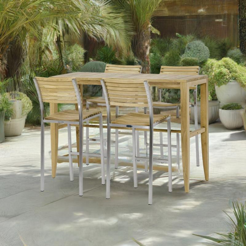 alt="70648 Laguna Vogue Teak Bar Set of Laguna Teak Rectangular Bar Table and 4 Vogue Teak and Stainless Steel Bar Stools angled on stone patio with potted plants and trees in the background"